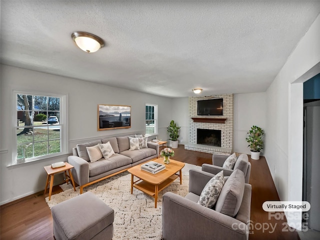 living area with a brick fireplace, a textured ceiling, and wood finished floors