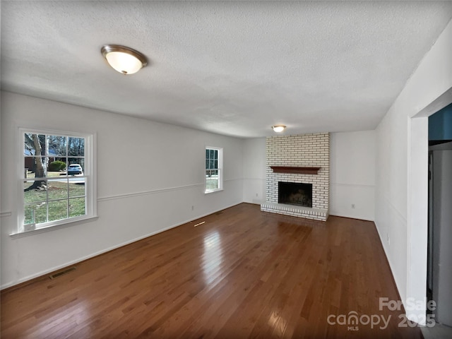 unfurnished living room featuring a textured ceiling, dark wood-type flooring, a brick fireplace, and visible vents