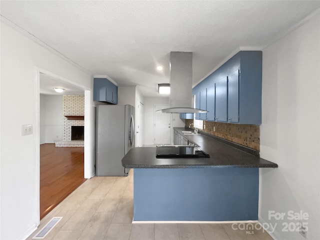 kitchen featuring a peninsula, blue cabinetry, island exhaust hood, and freestanding refrigerator