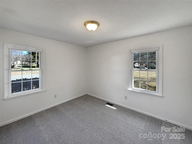 carpeted spare room with baseboards, visible vents, and a textured ceiling