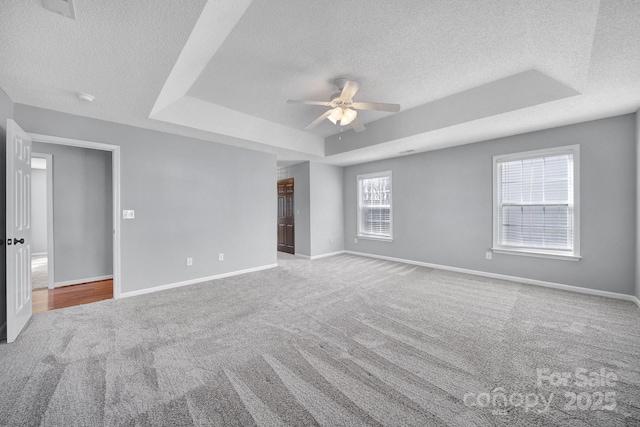 empty room with ceiling fan, carpet floors, a tray ceiling, and baseboards