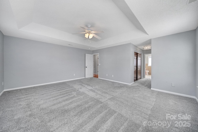 carpeted empty room with a textured ceiling, ceiling fan, a tray ceiling, and baseboards