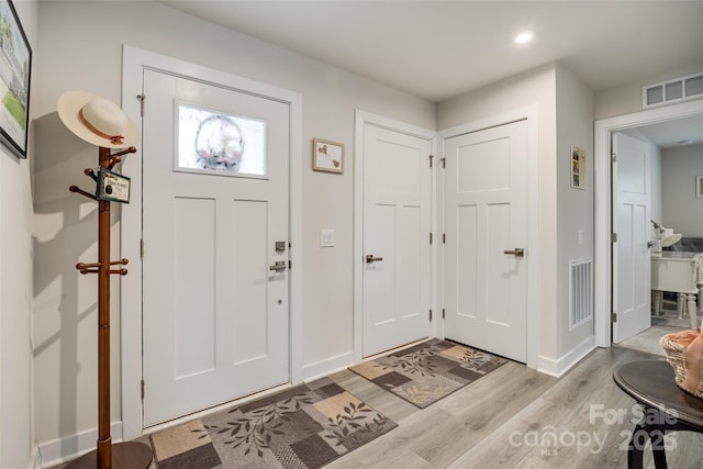 entryway with light wood finished floors, visible vents, and baseboards