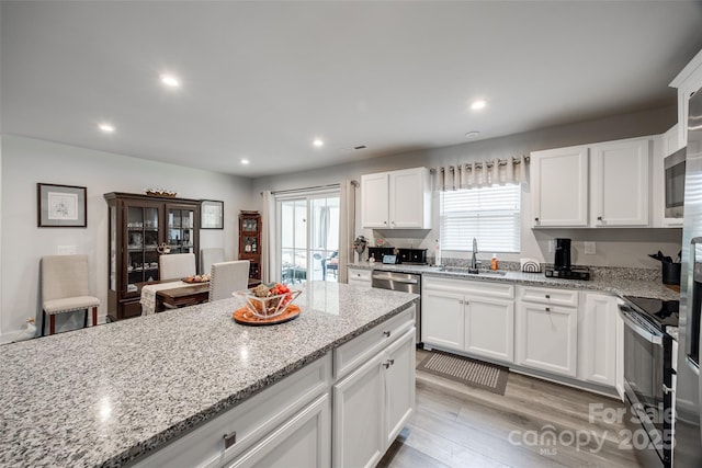 kitchen featuring light wood-style flooring, appliances with stainless steel finishes, light stone countertops, white cabinetry, and a sink