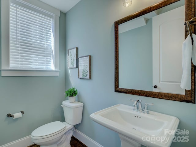 half bathroom with baseboards, a sink, and toilet