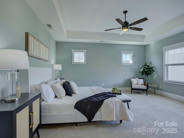 carpeted bedroom featuring a ceiling fan, visible vents, a tray ceiling, and baseboards