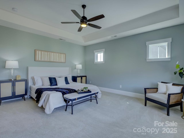 carpeted bedroom featuring visible vents, baseboards, a raised ceiling, and a ceiling fan