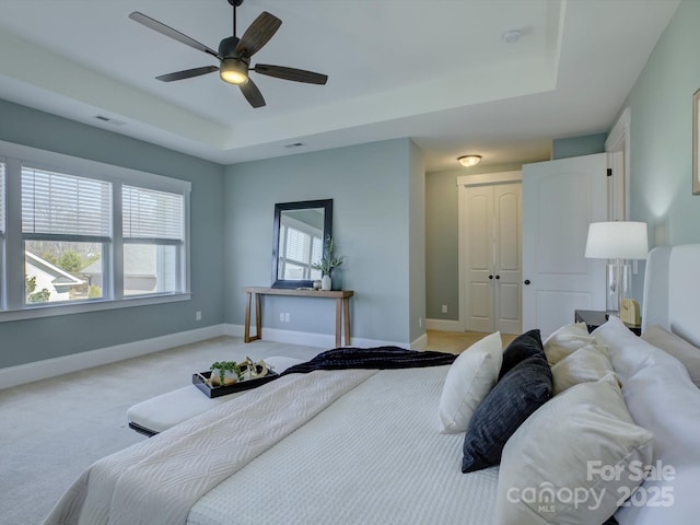 bedroom with a tray ceiling, a closet, light colored carpet, and baseboards