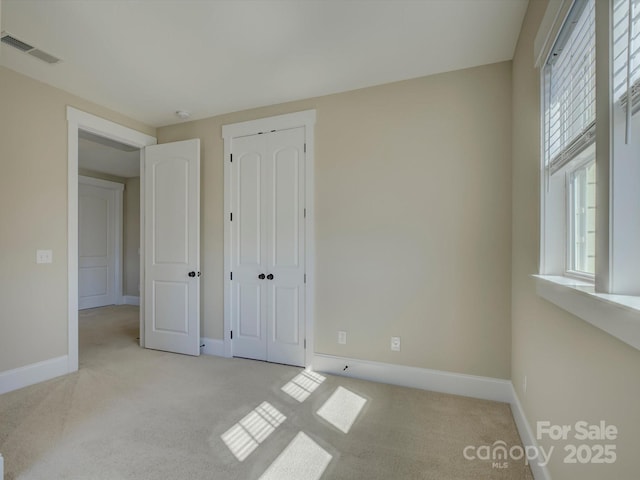 unfurnished bedroom with a closet, light colored carpet, visible vents, and baseboards