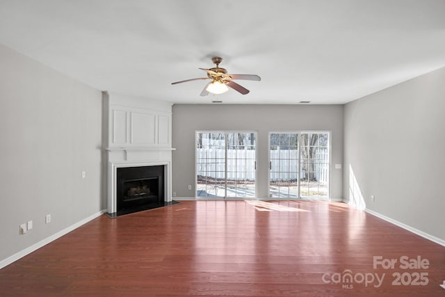 unfurnished living room featuring a fireplace, baseboards, and wood finished floors