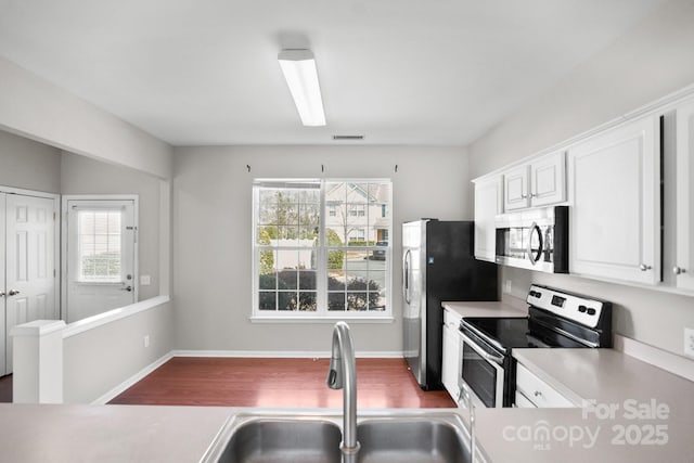 kitchen with white cabinets, appliances with stainless steel finishes, wood finished floors, light countertops, and a sink