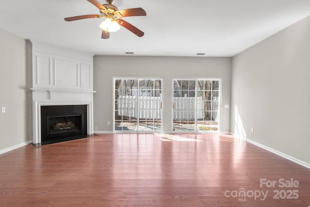 unfurnished living room with visible vents, a fireplace, baseboards, and wood finished floors