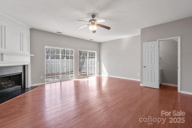 unfurnished living room with baseboards, visible vents, ceiling fan, wood finished floors, and a fireplace