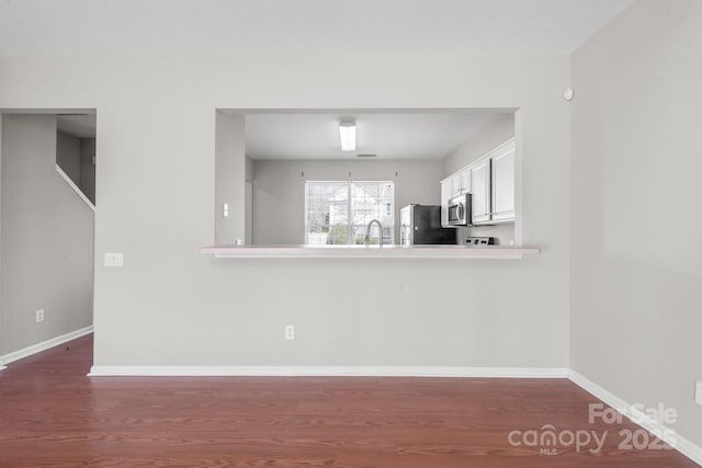 kitchen featuring baseboards, stainless steel microwave, wood finished floors, and freestanding refrigerator