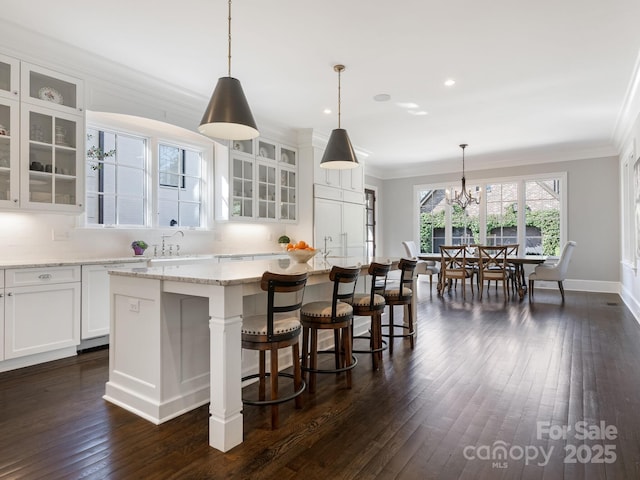 kitchen featuring white cabinets, dark wood-style floors, a kitchen island, crown molding, and a sink