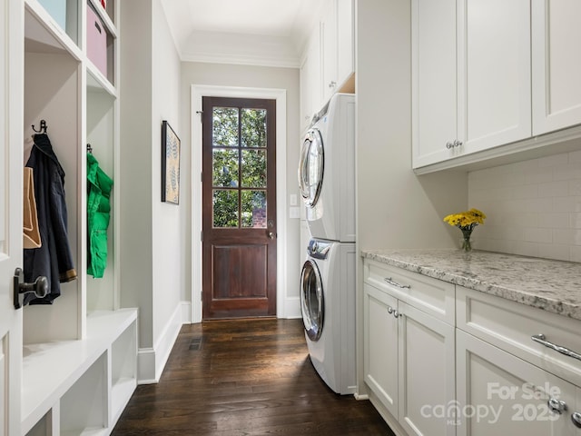 clothes washing area with dark wood-style flooring, baseboards, cabinet space, stacked washer and clothes dryer, and crown molding