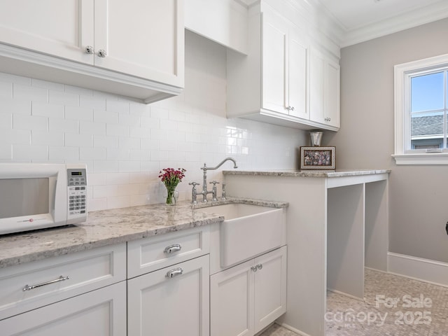 kitchen featuring tasteful backsplash, white microwave, ornamental molding, white cabinetry, and a sink