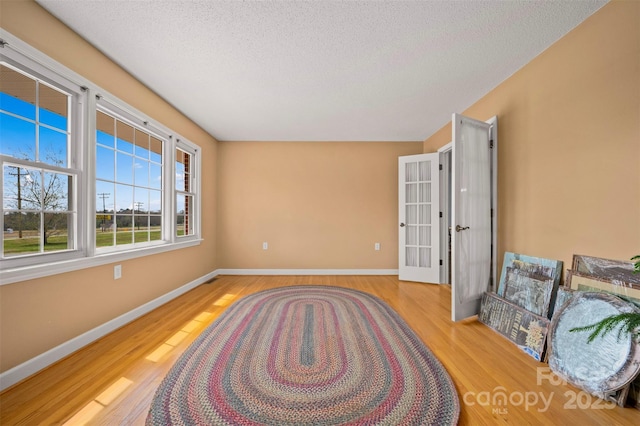living area featuring baseboards, a textured ceiling, wood finished floors, and french doors