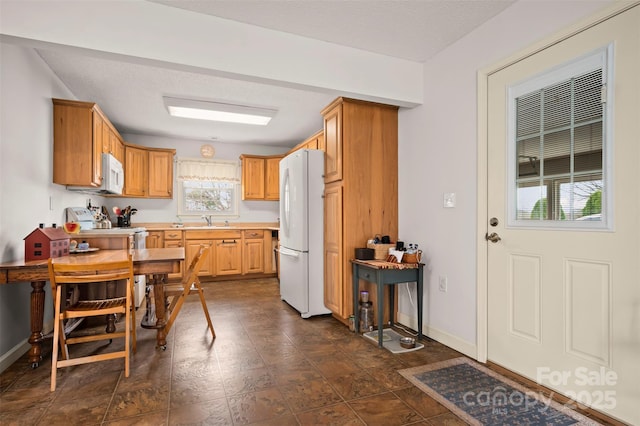 kitchen with a textured ceiling, light countertops, white appliances, baseboards, and a sink