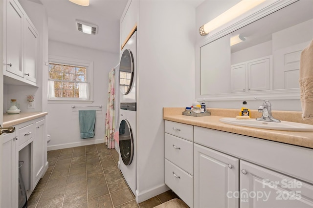 full bath with toilet, vanity, stacked washer and clothes dryer, baseboards, and visible vents