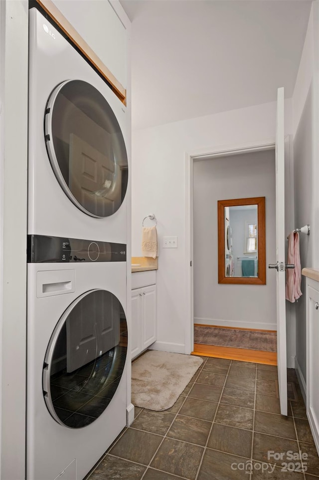 laundry room featuring baseboards, cabinet space, and stacked washer / dryer