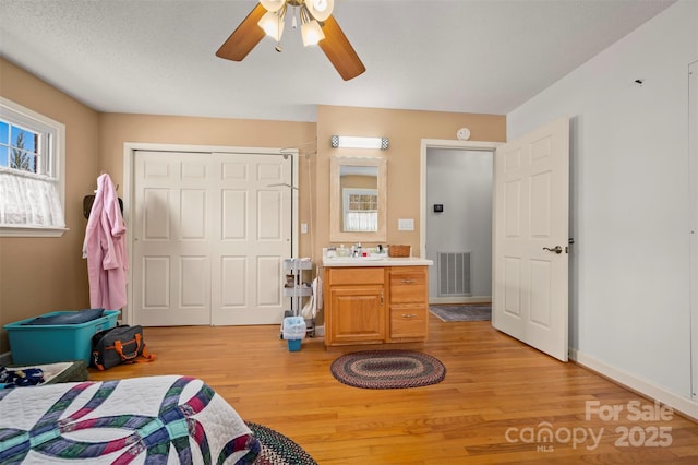 bedroom with a sink, light wood finished floors, visible vents, a ceiling fan, and a closet