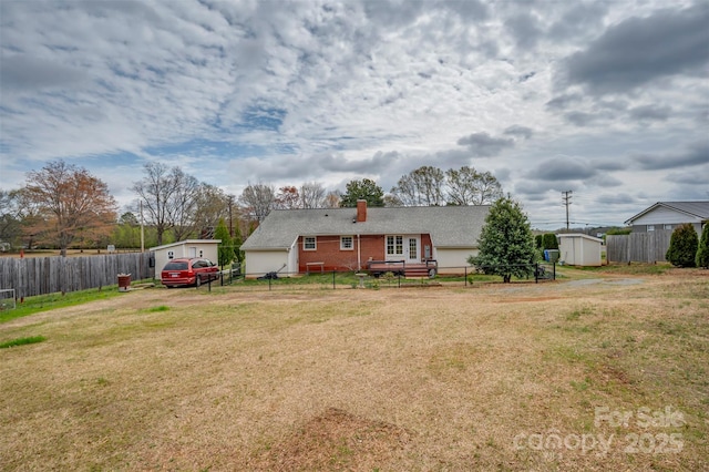 back of house with a chimney, an outbuilding, a storage shed, a fenced backyard, and a yard