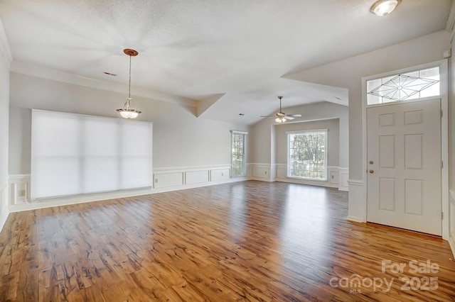 interior space with a ceiling fan, vaulted ceiling, wood finished floors, and wainscoting