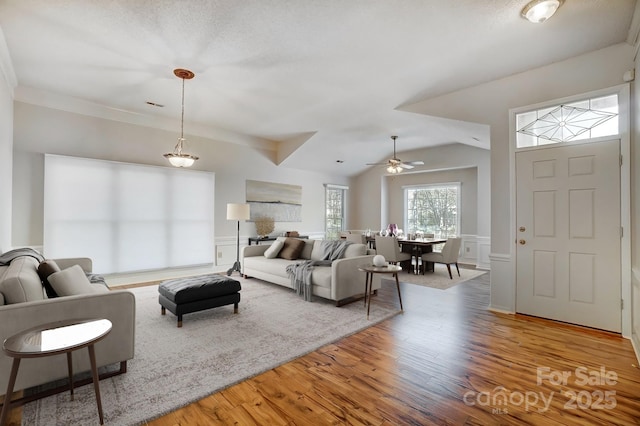 living area featuring lofted ceiling, wainscoting, light wood-type flooring, and a decorative wall