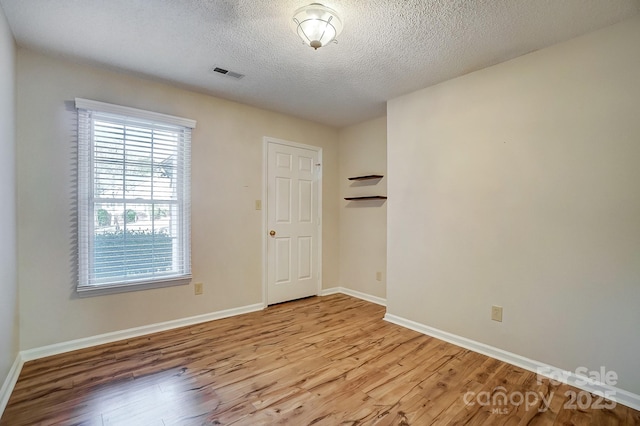 spare room with light wood-type flooring, baseboards, visible vents, and a textured ceiling