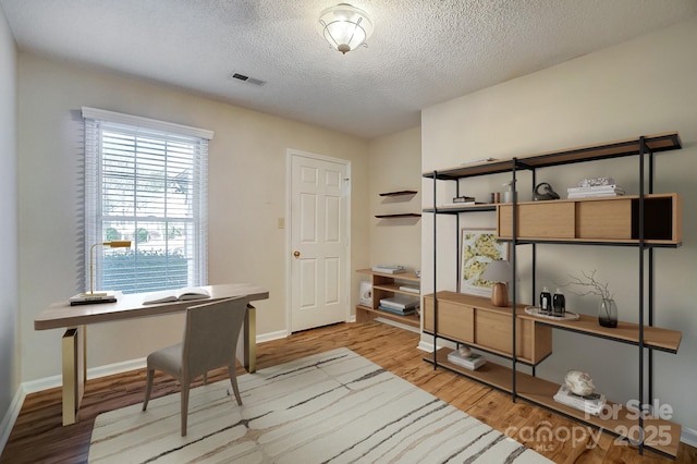 office with a textured ceiling, light wood-style flooring, visible vents, and baseboards