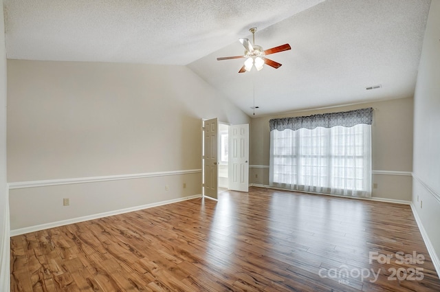 spare room featuring vaulted ceiling, wood finished floors, visible vents, and a ceiling fan