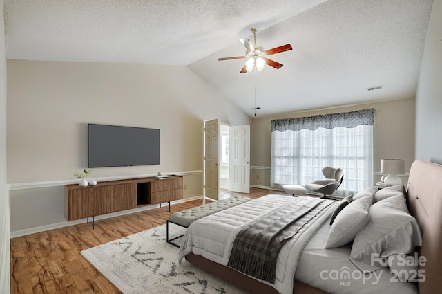 bedroom featuring ceiling fan, a textured ceiling, wood finished floors, visible vents, and vaulted ceiling