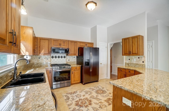 kitchen with light stone counters, a sink, appliances with stainless steel finishes, decorative backsplash, and brown cabinetry