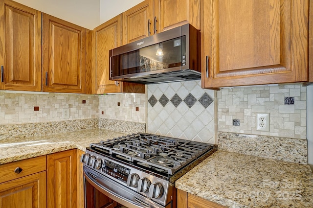 kitchen with light stone countertops, stainless steel gas range, brown cabinets, and decorative backsplash