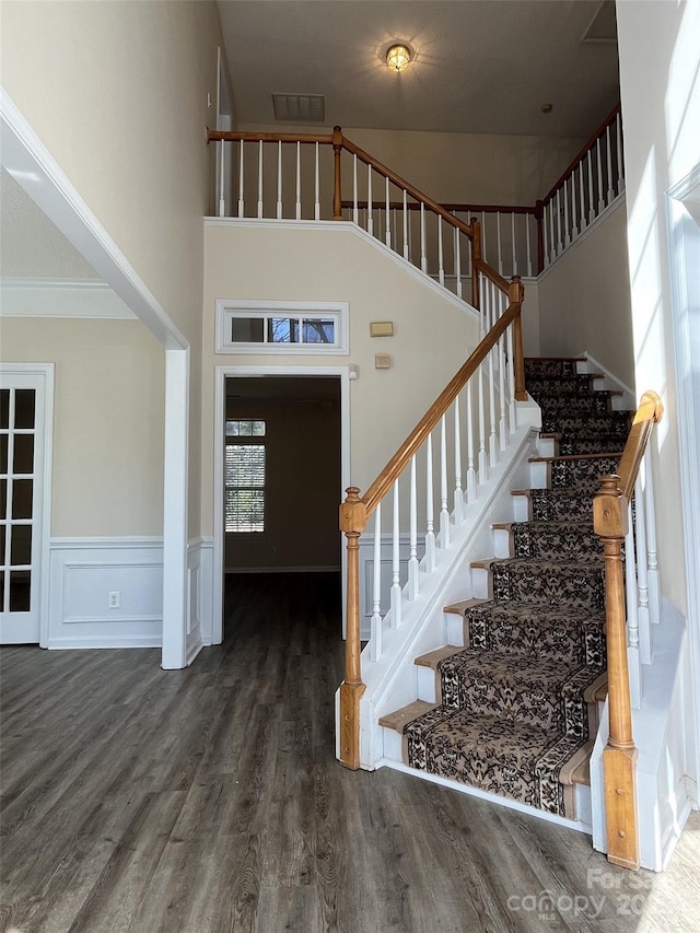 stairs featuring a wainscoted wall, a high ceiling, wood finished floors, and visible vents