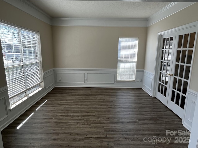 spare room featuring dark wood-type flooring, a wainscoted wall, ornamental molding, and a textured ceiling