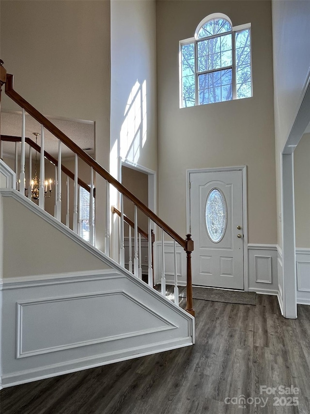 entryway featuring a wainscoted wall, dark wood finished floors, a decorative wall, stairway, and a towering ceiling