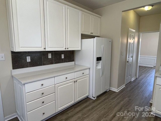 kitchen with light countertops, white refrigerator with ice dispenser, dark wood-style flooring, and white cabinetry