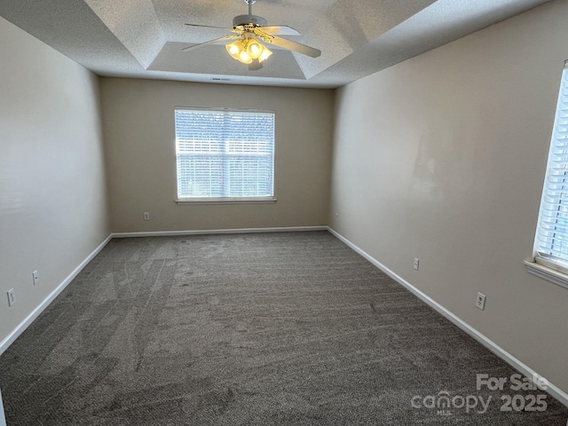 empty room with a textured ceiling, dark carpet, a raised ceiling, and baseboards