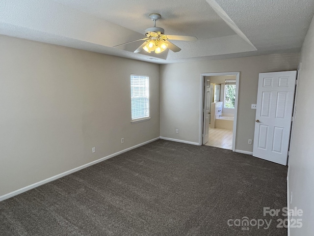 spare room featuring a healthy amount of sunlight, dark carpet, a textured ceiling, and baseboards