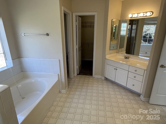 bathroom with baseboards, tile patterned floors, a garden tub, a spacious closet, and vanity