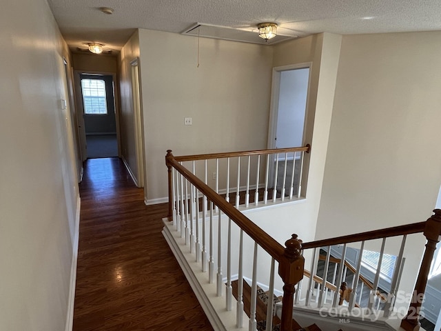 hallway featuring dark wood finished floors, attic access, a textured ceiling, an upstairs landing, and baseboards