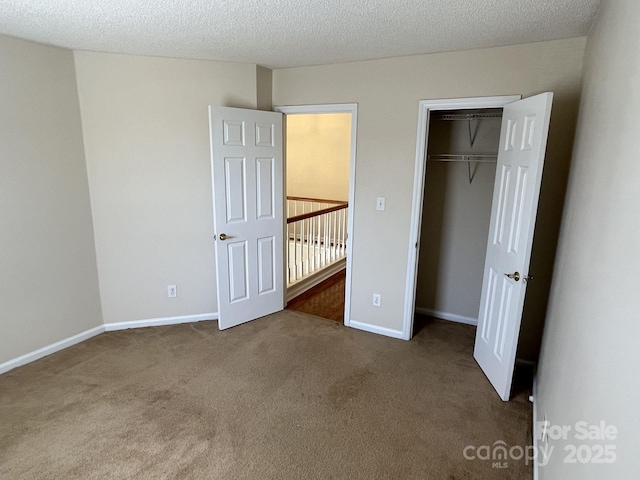 unfurnished bedroom with a textured ceiling, carpet floors, a closet, and baseboards