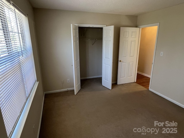 unfurnished bedroom with carpet floors, a textured ceiling, baseboards, and a closet