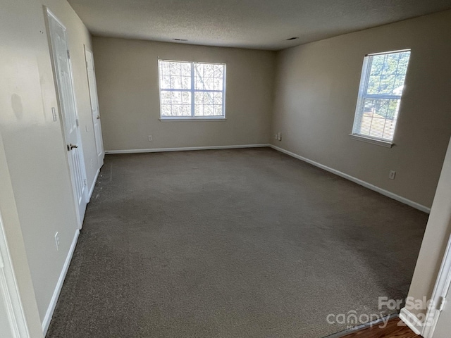 empty room featuring baseboards, plenty of natural light, dark carpet, and a textured ceiling