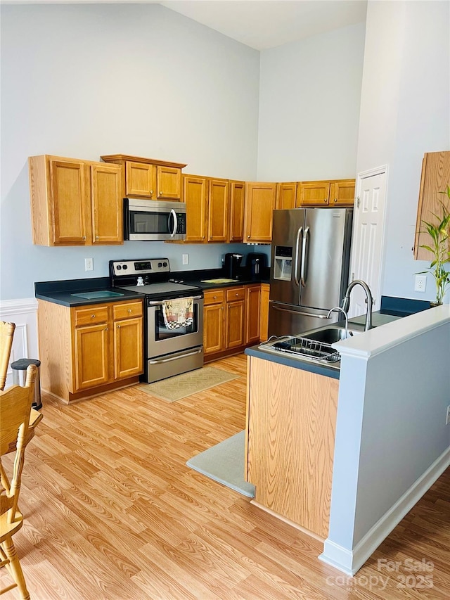 kitchen with stainless steel appliances, light wood-type flooring, high vaulted ceiling, and brown cabinets