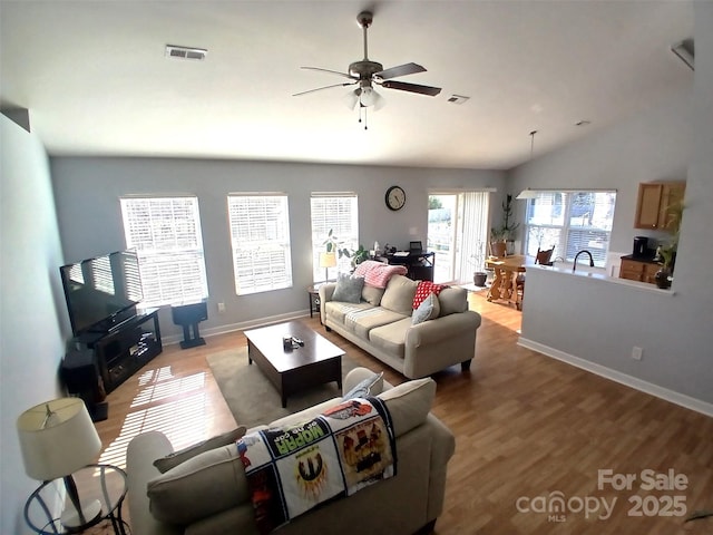 living room with ceiling fan, visible vents, baseboards, vaulted ceiling, and light wood finished floors