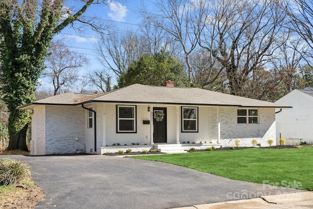 ranch-style house featuring brick siding, a shingled roof, driveway, a chimney, and a front yard