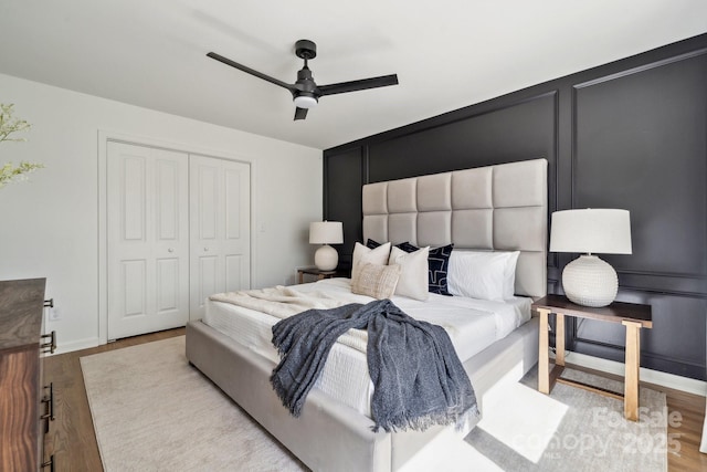 bedroom with a decorative wall, wood finished floors, a ceiling fan, baseboards, and a closet